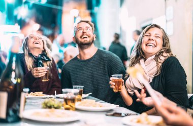 Mutlu arkadaşlar sokak festivalinde beyaz şarap içerken eğleniyorlar - gençler açık hava restoranında yerel yemekleri yiyorlar - sicim ışığı filtresinde akşam yemeği konsepti