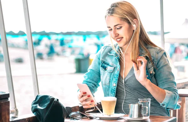 若い女性がコーヒーバーで携帯電話でビデオを見て ファッションブロガーの女の子がラテを飲みながらコンテンツを共有 ソーシャルメディアネットワーク上の現代的なさまようライフスタイルの概念 Azureフィルタ — ストック写真