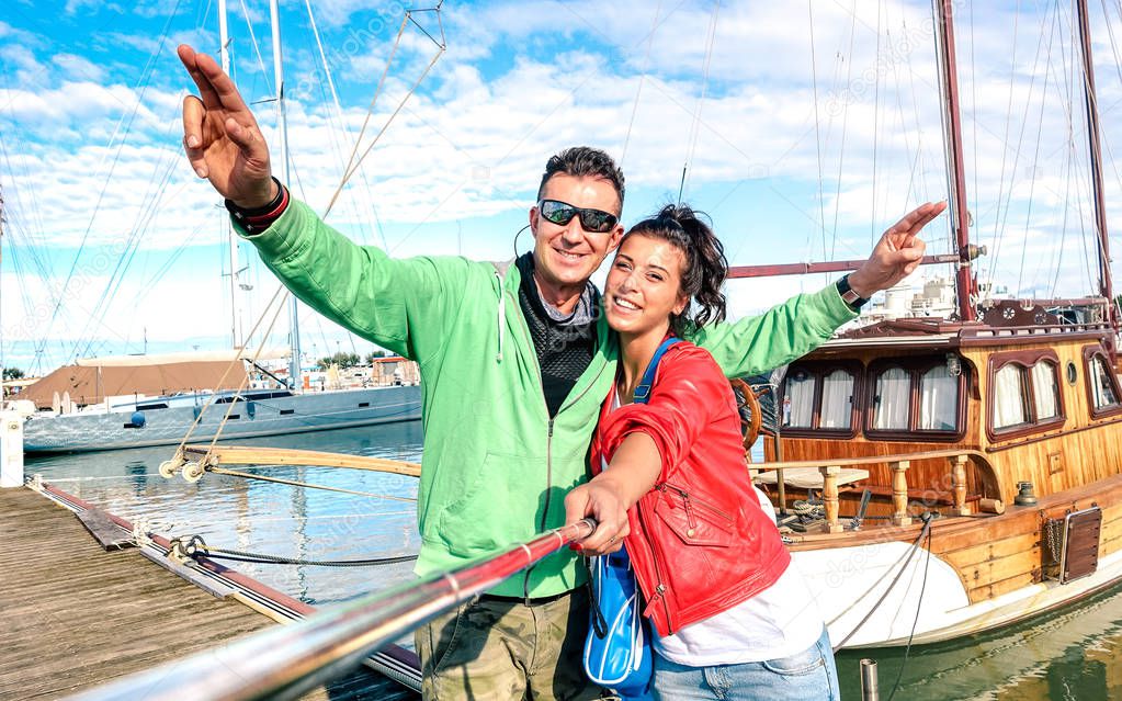 Young couple of lover taking selfie at sailboat docks on tour around world - Love concept  with happy boyfriend and girlfriend at honeymoon cruise on luxury boat experience - Bright vivid filter