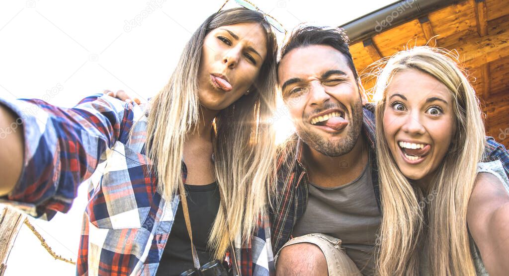 Friends trio taking selfie at trekking excursion - Happy friendship and freedom concept with young millenial people having fun together with funny faces on outdoors experience - Warm backlight filter