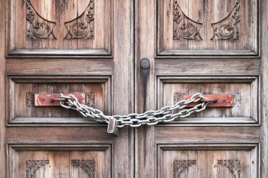 A double wooden door chained closed. Closeup of old wooden door with closed padlock on a chain. A chain of silver color with closed padlock on an old gate