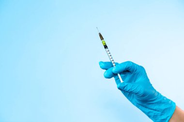 Mavi eldiven, açık mavi arka planda enjeksiyon için plastik şırınga ve sıvı tutuyor. Sağlık hizmetleri, tedavi uzmanları