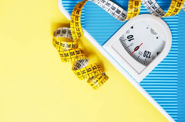 Blue weight scale and tape measure on yellow background. Sport equipment. Healthy lifestyle and diet concept. Yellow and light blue. Copy space