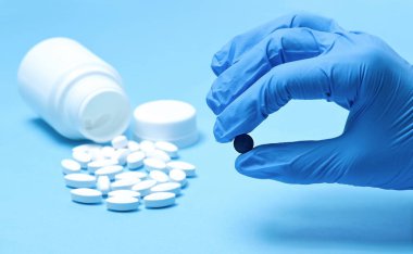 Beyaz haplar ve elinde mavi eldivenli siyah bir hap. Farklı haplar. Fotokopi alanına sahip açık mavi kağıt arkaplanı tıbbi ve farklı kavramları.