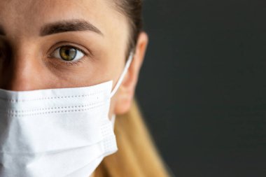 Tıbbi koruyucu maskeli, karanlık geçmişli, hasta bir kıza yakın çekim. Enfeksiyon kontrolü kavramı. Tıbbi konsept.