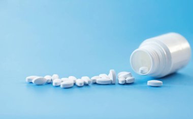 Beyaz şişeden dökülen haplar açık mavi arka planda fotokopi alanı ile birlikte. Tıbbi ve Küresel Sağlık Hizmetleri konsepti. İlaç endüstrisi.