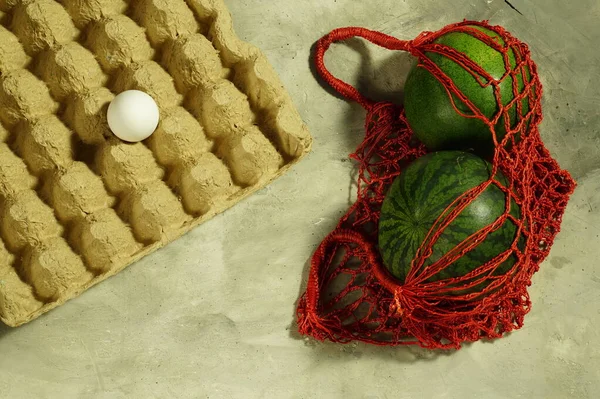 Saco de corda de saco de vime com duas melancias listradas e um ovo em um carrinho de papelão . — Fotografia de Stock