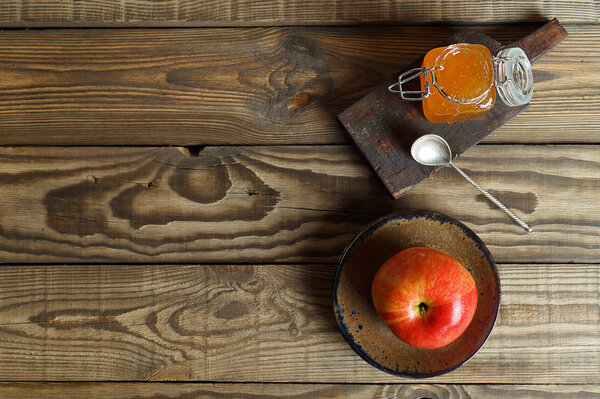 Red Apple on a plate and a jar of honey on a wooden background, top view.