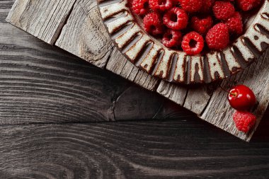        Freshly picked, red, raspberry berry lies in a ceramic plate on a wooden background. Next to two berries: raspberries and cherries. Copy space, top view.                     