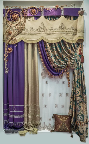 A luxury design of curtains in the east style. A gold, purple, green color curtain fabrics and lightweight translucent tulle with ornament.