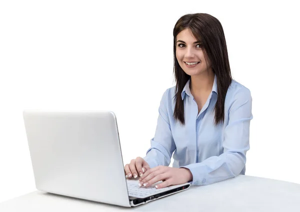 Una chica atractiva sonríe sentada en la mesa de la oficina. Ella está escribiendo texto en el teclado del ordenador portátil. Fondo aislado blanco . — Foto de Stock