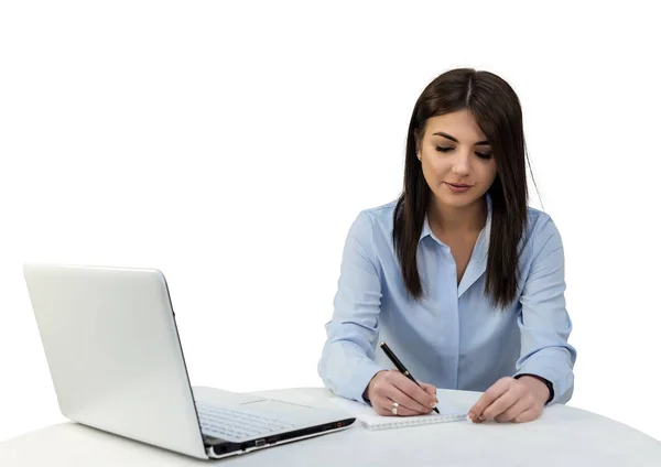 Chica joven sentada en la oficina con un ordenador portátil y está escribiendo en un cuaderno. Fondo aislado blanco . — Foto de Stock