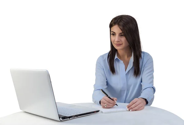 Una chica joven mira en un ordenador portátil y está escribiendo en un cuaderno. Fondo aislado blanco . — Foto de Stock