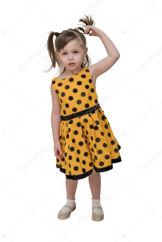 A small, mischievous girl in a bright yellow dress with polka dots, winds her hair around her hand. White isoolet background.