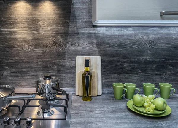 Cocina moderna en estilo Loft y acentos de color verde brillante en forma de tazas, manzanas y uvas. La encimera de gas está construida en la encimera de madera. Delantal de madera oscura áspera — Foto de Stock