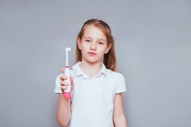 Küçük tatlı kız gülümser ve dişlerini gri bir arka planda renkli bir fırçayla fırçalar. Diş hijyeni. Mutlu küçük kız dişlerini fırçalıyor.