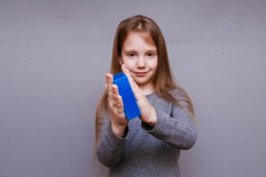 Elinde sabun ve sağlık maskesi olan gri arka planda küçük bir kız.