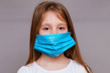 Gri arka planda, tıbbi maskeli küçük bir kız.
