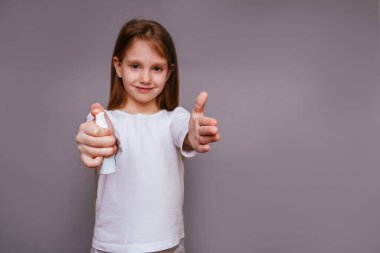 Beyaz ceketli, gri arka planda uzun saçlı bir kız elinde antiseptik tutuyor.