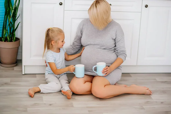 Pregnant Girl Sits Little Blonde Girl Floor Kitchen Cups Her — Stock Photo, Image