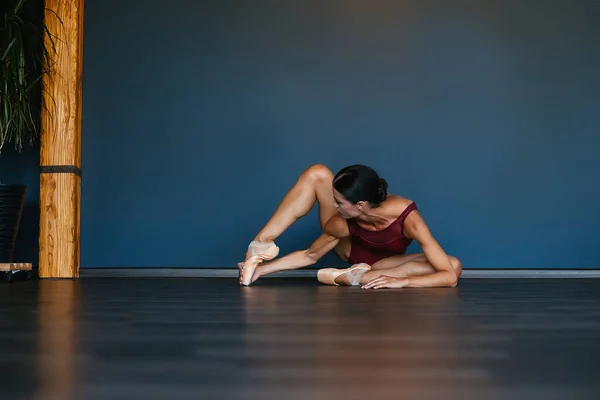 Danseuse de ballet moderne exécutant un exercice de ballet sur fond de studio sombre. Danseuse dans un justaucorps bordeaux rouge foncé — Photo