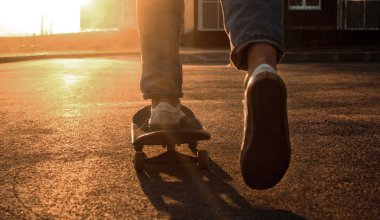 Kaykaycı bacakları yakın. Kaykaylı, kot pantolonlu ve spor ayakkabılı bir adam şehirde geziyor. Ekstrem şehir sporu. Güneş ışığı fotoğrafçılığı. Metin için boşluk.