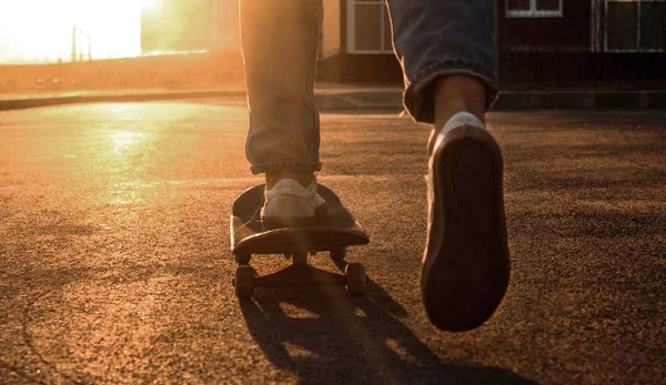 Kaykaycı bacakları yakın. Kaykaylı, kot pantolonlu ve spor ayakkabılı bir adam şehirde geziyor. Ekstrem şehir sporu. Güneş ışığı fotoğrafçılığı. Metin için boşluk.