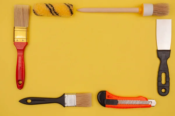 Sarı arka plandaki boya aletinin çerçevesi. Paten ve fırça, boya bıçağı ve bir spatula..