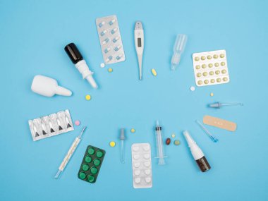Mavi arka planda hastalıkların tedavisi için tıbbi malzemeler. Yukarıdan manzara. İğneler, haplar, termometreler, pipetler, vs..