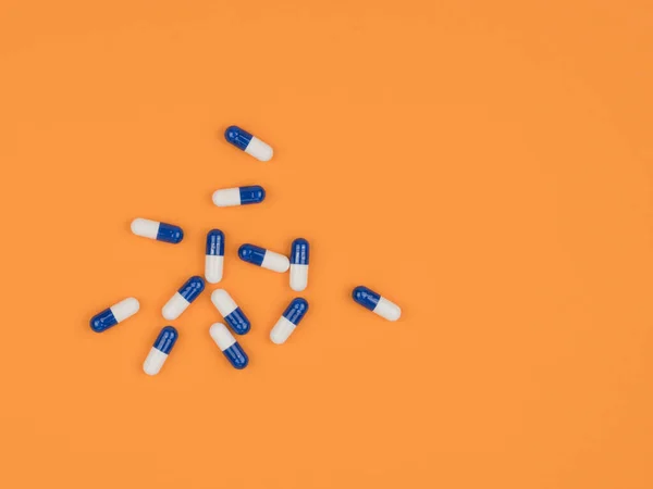 Medicine to treat on an orange background. Blue and white capsule.