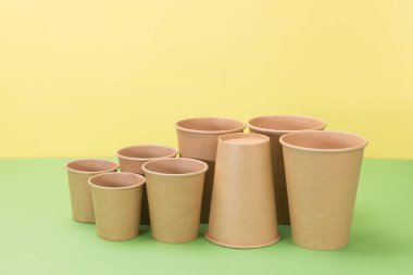 Sarı ve yeşil arka planda tek kullanımlık kağıt eşyalar. Farklı boyutlarda bir sürü bardak..