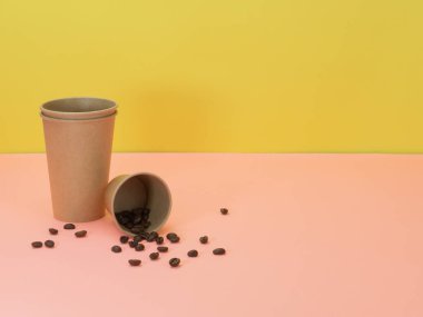 Pembe ve sarı arka planda kağıt fincanlar ve kahve çekirdekleri. Kahve, çay ve diğer içecekler için tek kullanımlık sofra takımı.