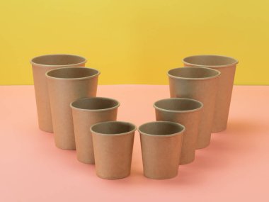 Pembe ve sarı arka planda çevre dostu kağıt bardaklar. Biyo yazılımı.