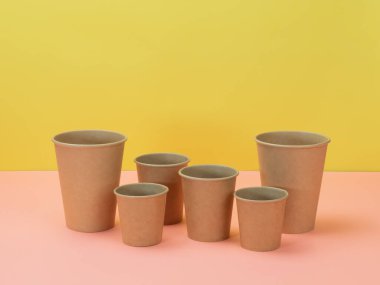 Pembe ve sarı arka planda çevre dostu tek kullanımlık sofra takımı. Kağıt bardaklar.