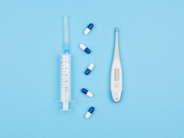 Mavi arka planda şırınga, uyuşturucu ve elektronik termometre var. Yukarıdan manzara. Hastalıkların tedavisi.
