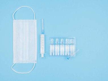 Maske, şırınga ve ampul mavi arka planda. Yukarıdan görünüşü.