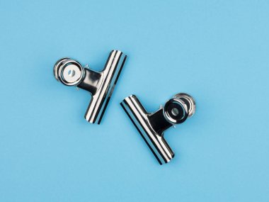 Mavi arkaplandaki kağıt için metal ataç. Yukarıdan manzara. Kağıt çizimi için klips.