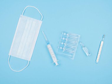 Maske, termometre, şırınga ve ampul mavi arka planda. Yukarıdan görünüşü.