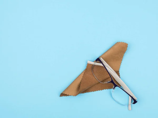 Óculos e um pano para limpar lentes em um fundo azul . — Fotografia de Stock