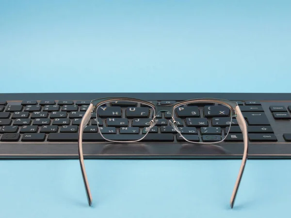 Glasses and keyboard on a blue background. — Stock Photo, Image