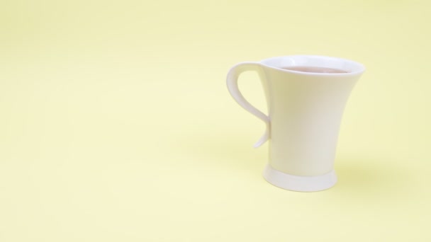 Alta taza blanca de té sobre un fondo amarillo . — Vídeos de Stock