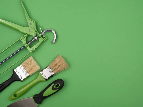 Green painting tool on a green background. The view from the top. Gun, trowel and brush.