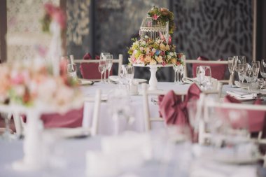 Vazolarında pembe çiçekler olan düğün süsü. Misafirler için masa, çatal bıçak, çiçek ve çanak çömlek ile servis edilir ve masa örtüsüyle kaplanır. Zarif tablo manzarası.