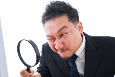 Genç işadamı masada otururken büyüteçle bilgisayara bakıyor. 