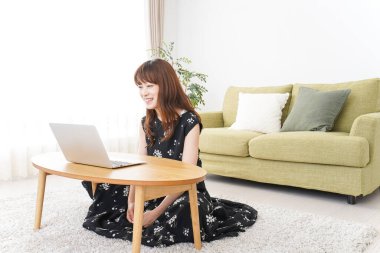 Genç Asyalı kadın evde dizüstü bilgisayar kullanıyor, internetten iletişim kuruyor. 