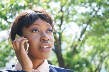 Genç Afrikalı iş kadını parkta cep telefonuyla konuşuyor.