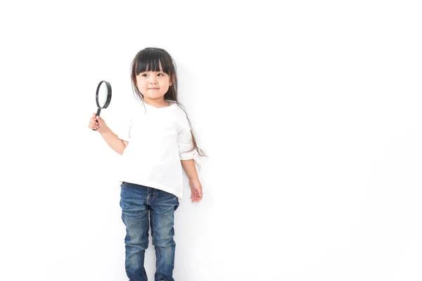 亚洲小女孩拿着用白色背景隔开的放大镜 — 图库照片