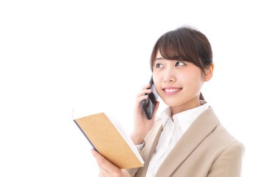 Not defterli Asyalı iş kadını beyaz arka planda cep telefonuyla konuşuyor.