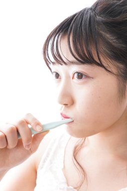 Beyaz arka planda dişlerini fırçalayan genç Asyalı kadın.