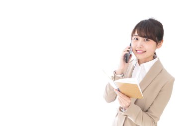 Not defterli Asyalı iş kadını beyaz arka planda cep telefonuyla konuşuyor.